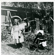 Dextra Baldwin on left, holding a large doll.  She has ribbons in her hair and is wearing a large hat.  Brother Baldwin M. Baldwin is sitting in a child's "walker-type" device and has white bonnet on.