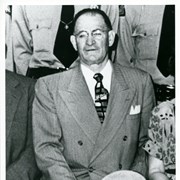 Photo of Arcadia Police Chief William Cahill (served 1947-1951), blown up from a group photo with other officers.  He is seated holding a hat and is wearing a suit and tie.
