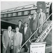 Seven men are standing near or on stairs leading to a Western Airlines airplane.  A sign reads WESTERN AIRLINES PRESENTS THE CALIFORNIAN. Charles Eaton is on the right, wearing a hat and holding the railing.