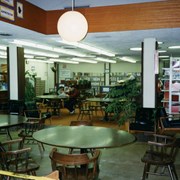 Phase I of Library Renovation/Expansion project at 20 W. Duarte Road. Temporary adult reading area with round tables are seen in what used to be the Children's Room. Microfiche/film cabinets are visible along wall to the left. Several patrons are seen sitting at the tables.