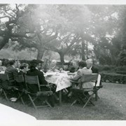A garden party at the Burnell Estate with ten people seated at a table outside on the lawn.  George Edwin Burnell is seated at the head of the table.