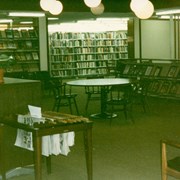 View inside Arcadia Public Library, 20 W. Duarte Road shortly before the start of construction for the 1995/96 expansion/remodel project.  This photo is of the periodicals area.  There is an empty round table and chairs in the center of the area.  The old fiction section is visible to the back right.