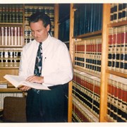 Arcadia City Manager Bill Kelly is seen standing in front of book cases in the office of the City Attorney.  He is wearing a white shirt and tie and is looking down at a book in his hands.  Photo was taken by Dorothy Denne of the Arcadia Weekly to be used in a display at the Library for National Library Week.