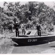Three men are standing on a small boat during filming of a movie at the Arboretum.  Handwritten note states,"John Payne in Enchanted Voyage - July, 1945 - Rancho Santa Anita."
