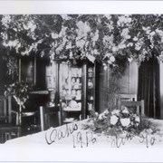 Interior of Clara Baldwin Stocker's home on Foothill Boulevard in Arcadia.  There is an arrangement of flowers on the table and a large amount of flowers along the top of the photo.  Handwriting along the bottom of the photo reads, "Oaks 1915 dinner table."