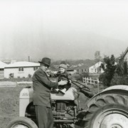 Charles Francis Earl is seen standing next to a tractor, holding his young son, William Earl.  Behind the Earl's is the vacant lot Mr. Earl purchased in the mid 1930s when it was a hayfield.  The vacant lot as seen in this photo is shortly before construction began on their home in late 1951 and early 1952. When constructed, the address was 1050 Paloma Drive.  See also Photo #1634.