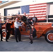 City Department Heads pose with vintage Arcadia Fire Department truck, each one wearing a fire department hat. From left to right: Don Penman, Jerry Collins, Dave Hinig, Bill Kelly (behind steering wheel), Tracy Hause, Pat Malloy, Janet Sporleder (seated on running board).