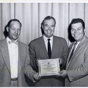 Three men in suits, holding a National Safety Council Award for the Arcadia Police Department. Date on award reads 1955-1956. Man on the right is Eric Topel. See also photo ID 1768.