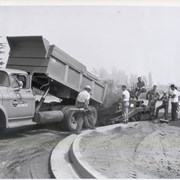 Construction in progress of the one-story Arcadia Police Department building at 250 W. Huntington Drive. Truck is unloading materials while workers look on. "Osborn Co. Grading - Paving, Pasadena" is the name on the truck.