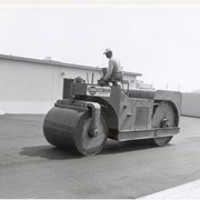 Man driving and operating a steamroller, or road roller, used to level roads on the construction site of the one-story Arcadia Police Department building at 250 W. Huntington Drive. Name on the steamroller reads: Osborn Co. Contractors, Pasadena.