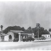 West Arcadia Service Station, designed in Spanish style architecture including red tile roof located at 1221 S. Baldwin, was operated by Bruce Wetmore and Blake Smith.  Man working on car is Bruce Wetmore. Shell Gasoline. Gilmore Red Lion.