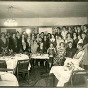 Group picture of about 36 unidentified women. All appear to be wearing dresses. Part of a brick fireplace is visible. There are tables and chairs set up for a meal or party. An attached note read "Mrs. Woodward 2nd, 212 S. Third, 447-5236" so librarian has written that on the back of the photo.