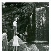 Three youngsters are seen admiring the new man-made waterfall installed on Tallac Knoll at the Arboretum.  None are identified.