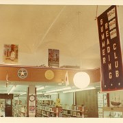 Children's Room, Arcadia Public Library, 20 W. Duarte Rd. decorated with Summer Reading Club banner and 1968 Summer Olympics theme with flags and emblems of various nations. Architectural details such as arched ceiling and light fixtures (hanging globe pendant light), and shelving, Mayflower ship model are visible.