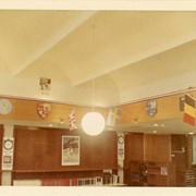 Children's Room, Arcadia Public Library, 20 W. Duarte Rd. decorated for Summer Reading Club with 1968 Summer Olympics theme, featuring flags and emblems of various nations. Architectural details such as arched ceiling and light fixtures (hanging globe pendant light), and shelving, atlas case, and doors are visible.