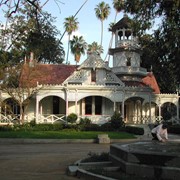 Queen Anne Cottage with red trim, at the Los Angeles County Arboretum. A fountain in the foreground and palm trees in the background. A person is hunched over the edge of the fountain. Arboretum address is 301 North Baldwin Avenue, Arcadia, CA. Any use of this image must be credited "Photograph by David Stevens. Copyright David Stevens."