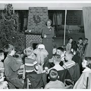 Group of youngsters photographed at Christmas party in Children's Room, Arcadia Public Library, 25 N. First Avenue.  Standing is Children's Librarian Marjorie Hickerson (later, Phelps).