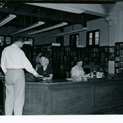 Eleanor Gilbert, library clerk on left at circulation desk, and Grace Rahm, library clerk on right of desk, at Arcadia Public Library, 25 N. First Avenue.  Person in white shirt being waited on.