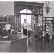 Eleanor Gilbert at circulation desk of Arcadia Public Library, 25 N. First Avenue.  View is looking east out front door.  Mother and son are coming in door.  Patron is browsing in 7 day book area.  Photo wide view of #308.