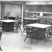 View of audiovisual area of library at 20 W. Duarte Road.  Pictured behind desk is Hazel Bolton.  One patron is listening to record on record player.  White file cabinets along wall on left side of photo.