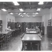 View of adult reading room at Arcadia Public Library, 25 N. First Avenue. Photo shows 2 men seated, one girl standing in stacks and one mother and child in stacks.