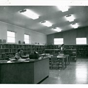 View across Children's Wing, Arcadia Public Library, 25 N. First Avenue. Shows one person at desk, seated, and another standing looking at book.  There is shelving along outside walls of room.