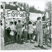 Crowd of children and adults are seen at a school carnival.  The Fish Pond booth is most prominent.  The school has not been identified.