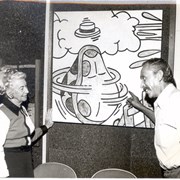 Vi Chaffers, on left, Children's Librarian at Arcadia Public Library, 20 W. Duarte Road. She is looking at large cartoon-part of art show in Art & Lecture Room.  Talking with her about piece is Gilbert Castruita, Library Custodian.