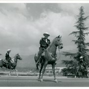 View north across Santa Anita Race Track parking lot toward San Gabriel Mountains with three members of Los Angeles County Sheriff's Posse mounted for Peach Blossom Festival.