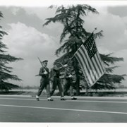 Three uniformed young men carrying large American flag at Peach Blossom Festival Parade as it passes in front of Santa Anita Race Track parking lot.