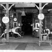 William Parker Lyon Pony Express Museum-entryway to exhibit room. Sign reads W. Parker Lyon, from which a bell hangs. Another sign reads Wells Fargo & Co Express. Watch or clock shaped signs read Ingersoll Watches and Sherrard Jeweler. Hobby horses and small wooden chairs on either side of the entrance. Print of this photo is in the W. Parker Lyon Pony Express Museum Scrapbook, Box 31, in History Room, Shelf B3.