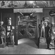 Indoor entrance to bar in Pony Express Museum.  Over the entrance is a sign reading: Butte City Saloon and on other side of entrance are signs reading: Hollenbeck Hotel Bar.  There are typical store-front carved figures standing on either side of door, which has double swinging doors.