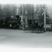 Photo looking west from in front of Pony Express Museum.  Shows portion of train, entire light-weight enclosed horse-drawn carriage.  The conifer trees which line Huntington Drive, near Santa Anita Race Track, can be seen.
