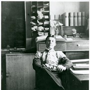 Young man with a paisley tie and high collar sitting at a desk.  There are what appear to be mail boxes above his head.  There is also a jar with Calla Lillies on ledge behind him.  Beneath him is printed: Santa Anita R.W. Station.  His identity was given as George Kennedy, Santa Fe and Wells Fargo Agent, by Sandy Snider in April of 1998.