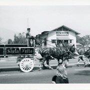 A handsomely painted wagon, for the Peach Blossom Parade, bearing SANTA ANITA on side, pulled by 4 work horses, is passing by a building with a sign for BARBOUR'S PRESERVING CO.  City Directory locates this business at 27 1/2 Huntington Drive.
