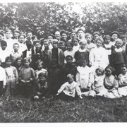 About 38 students and two teachers or possibly three are seated and standing in grass in front of trees or shrubs.  We believe the African-American boy is Julian Fisher.