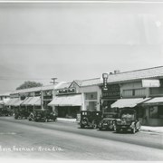 View of a section of Baldwin Avenue business district in the 1000 S. Baldwin block.  Eleven automobiles are diagonally parked in front of the various shops.