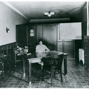 View of interior of Pacific Telephone Business Office showing one woman seated at a table.  There is a file cabinet, a typewriter, and a safe in the room.  Floor appears to be tiled.  Location of this office was on North First Avenue.
