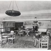 Interior of the Jinks room at Anoakia, showing circular hanging light fixtures and tables with chairs.  The tile floor is visible, as well as part of the Maynard Dixon mural.