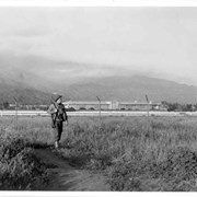 Military police patrol fence around Santa Anita Assembly Center.  Photo shows one soldier, and the Santa Anita Race Track Club House in background.