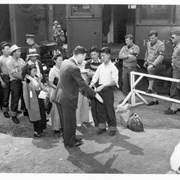 A doctor checks hand of evacuees as they line up near Pacific Electric Railroad cars which brought them to Santa Anita Assembly Center for the Japanese. Military personnel look on.