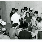 Medical staff administering health check-ups and giving inoculations.  Two persons are seated at a table, and nine others are giving shots or waiting for treatment at Santa Anita Assembly Center for the Japanese.