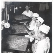 Four male kitchen helpers in white aprons and cap at Santa Anita Assembly Center for the Japanese, show 9 huge pans of what looks to be spaghetti ready to be served.
