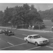 View of portion of Diamond Jubilee Parade along Campus Drive, shows white car, followed by vintage cars carrying, first, Councilman Charles Gilb, and second, former Councilwoman Floretta Lauber.