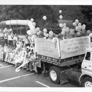 Truck pulling flat-bed trailer is loaded with people, balloons and signs promoting Arcadia Lions White Cane Days.