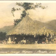 Thatched conical shaped roadside fruit stand with the name SLEMONS' ORANGE WIGWAM,ARCADIA,CALIF. According to 1930 City Directory, it was located at 141 E. Foothill Boulevard.  (McDonalds address in 1993 is 143 E. Foothill.) Owner was James B. Slemons.  Two people can be seen standing near entrance.