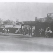 Looking north east toward intersection of Santa Anita Ave. near point where Campus Drive intersects.  McLean's Garage is plainly seen on the right.  A large gasoline truck is parked just to the north.  Farther north can be seen Arcadia Cash Market with another tank truck parked in front.  There are at least 9 people seen standing by; one, a police officer, third from right.