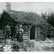 Man and lady (not identified) standing by small log cabin referred to as "Home of the 49er" on Baldwin's Ranch. It is said that Baldwin had it built to remind him of his background.