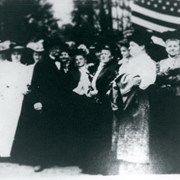 E.J."Lucky" Baldwin surrounded by bevy of ladies.  Ten women are seen surrounding him.  A large United States flag is seen on the right side. Occasion is not known.  Probably taken at Baldwin Ranch, Arcadia.