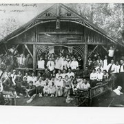 A large group is pictured sitting or standing near entrance to Sturtevant Camp dining room.  (Camp was one of many in San Gabriel Mountains; it was up Big Santa Anita Canyon.)  In back row, on left, man in dark shirt and tie next to pillar, is John C. Juvinall of Monrovia.
